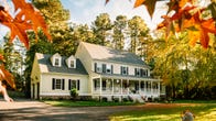 A two-story yellow house with a front porch surrounded by trees.