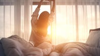 Woman stretching in bed after waking up to the morning sun.