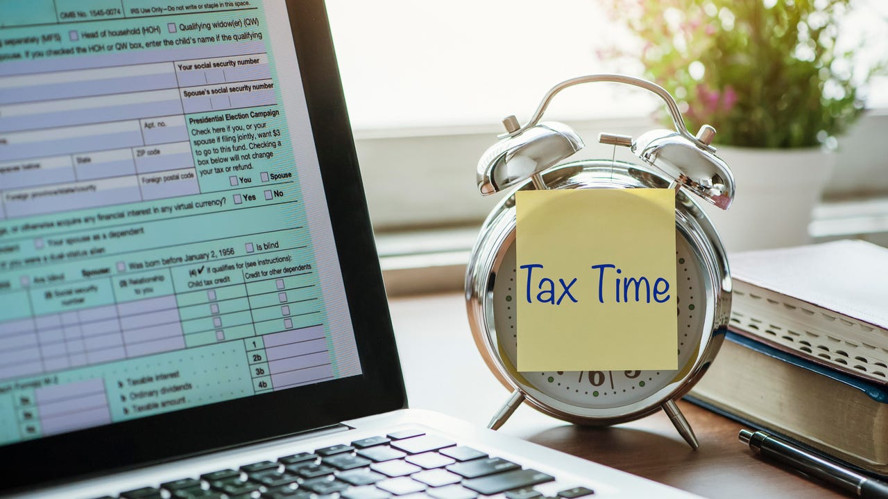 Old-school alarm clock with post-it reading tax time next to a laptop.