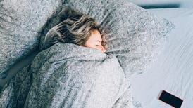 woman sleeping in bed with gray bedclothes, phone by her side