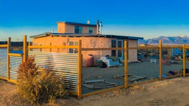 A stucco house behind a fence in the desert.