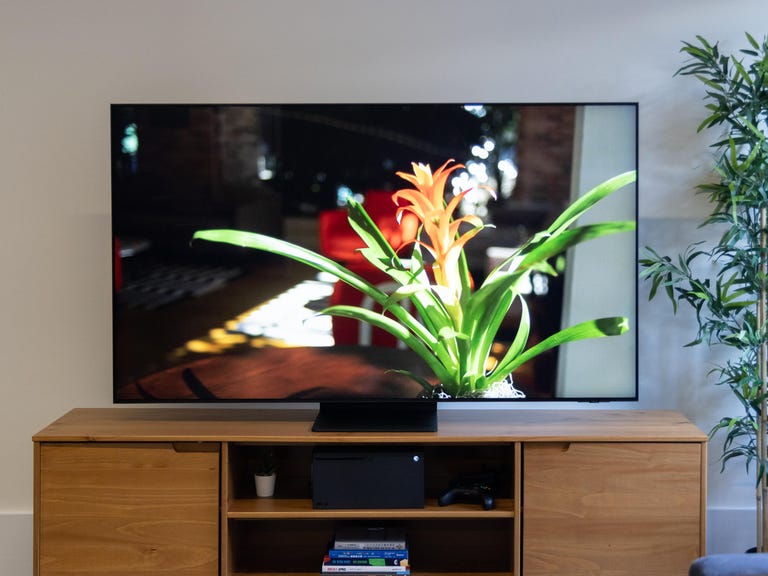 The Samsung QN90B QLED TV sits on a wooden tabletop stand.