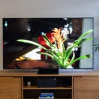 The Samsung QN90B QLED TV sits on a wooden tabletop stand.